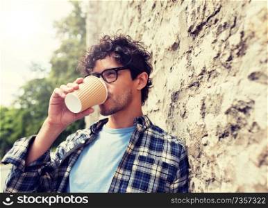 lifestyle, drinks and people concept - man in eyeglasses drinking coffee from disposable paper cup over stone street wall. man in eyeglasses drinking coffee over street wall