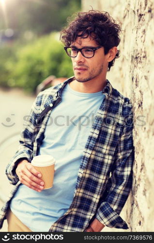 lifestyle, drinks and people concept - man in eyeglasses drinking coffee from disposable paper cup over street wall. man in eyeglasses drinking coffee over street wall