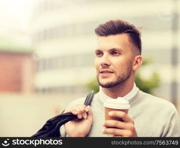 lifestyle, drinks and people concept - young man with bag drinking coffee from paper cup in city. young man with bag drinking coffee in city