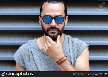 lifestyle, emotion, expression and people concept - man in sunglasses touching beard on city street