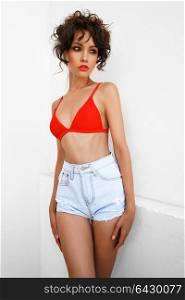 Lifestyle fashion photo of beautiful graceful woman in red bikini and jeans shorts. Spring Summer. Beach summer vibes. Travel season