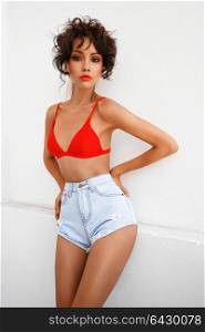 Lifestyle fashion photo of beautiful graceful woman in red bikini and jeans shorts. Spring Summer. Beach summer vibes. Travel season