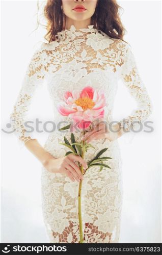 Lifestyle fashion photo of beautiful young woman in white lace dress with pink peony. Holidays and Events. Wedding. Valentine&rsquo;s Day. Spring blossom. Summer season.
