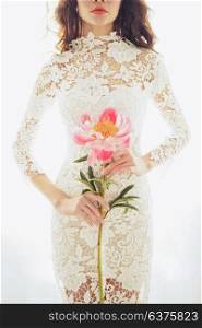 Lifestyle fashion photo of beautiful young woman in white lace dress with pink peony. Holidays and Events. Wedding. Valentine&rsquo;s Day. Spring blossom. Summer season.