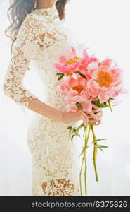 Lifestyle fashion photo of beautiful young woman in white lace dress with pink peony. Holidays and Events. Wedding. Valentine?s Day. Spring blossom. Summer season.