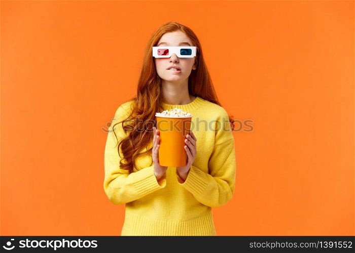 Lifestyle, hobby and people concept. Cute geeky redhead woman in 3d paper glasses, holding popcorn and biting lip as staring at favorite actor playing in movie, visit cinema to watch premiere.. Lifestyle, hobby and people concept. Cute geeky redhead woman in 3d paper glasses, holding popcorn and biting lip as staring at favorite actor playing in movie, visit cinema to watch premiere