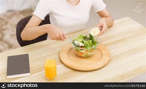 Lifestyle in living room concept, Young Asian woman mixing vegetable salad with salad dressing.