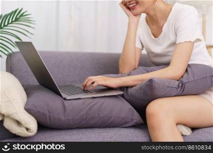 Lifestyle in living room concept, Young Asian woman sitting with hand on chin and using laptop.