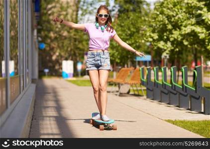 lifestyle, longboarding and people concept - smiling young woman or teenage girl in sunglasses riding on longboard along summer city street. happy teenage girl in shades riding on longboard