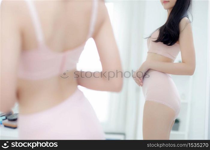 Lifestyle of beautiful young asian woman in underwear looking in mirror with belly figure slim at home, beauty body girl in lingerie shape fit with weight loss, abdomen and waist sexy perfect.