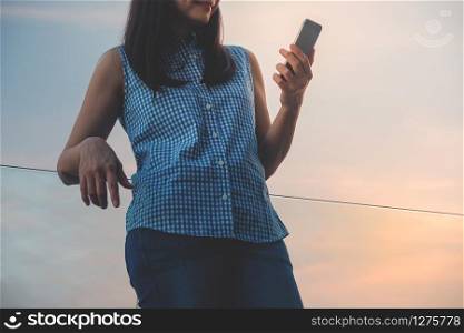 Lifestyle of Modern People Concept. Young Woman Relaxing by Reading Data or Message via Smartphone. Standing at the Deck by Riverside in Summer