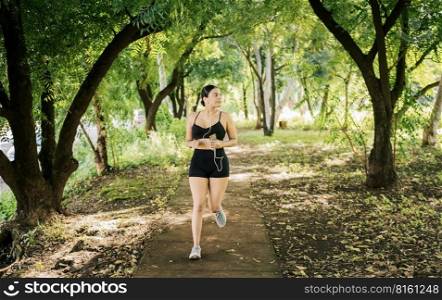 Lifestyle of sporty young woman running in a park surrounded by trees. Healthy lifestyle concept, Sporty young woman running in a park. A girl running in a park while listening to music
