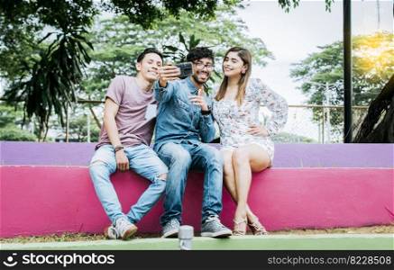 Lifestyle of three friends sitting in a park taking a selfie, Three teenage friends sitting in a park taking selfies. Meeting of three happy friends taking a selfie sitting in the park