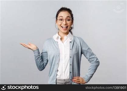 Lifestyle, people and emotions concept. Cheerful, happy asian woman in glasses introduce new company product or banner, pointing, holding promo on hand over left side copy space.. Lifestyle, people and emotions concept. Cheerful, happy asian woman in glasses introduce new company product or banner, pointing, holding promo on hand over left side copy space