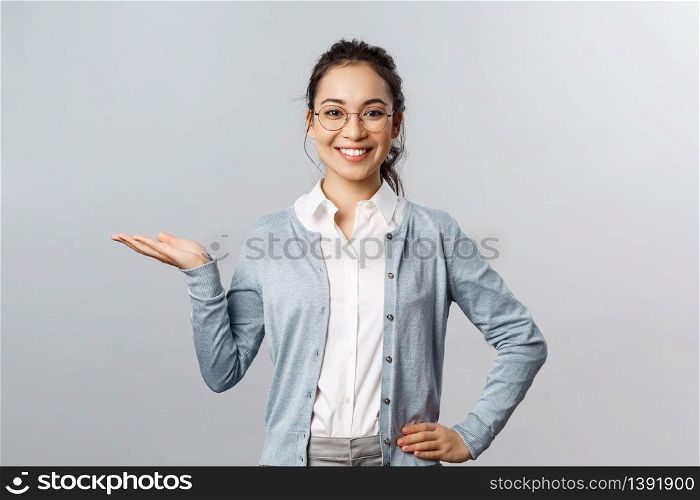 Lifestyle, people and emotions concept. Girl introduces product, recommend this. Portrait of attractive, confident smiling asian woman showing her chart or project on hand over left side.. Lifestyle, people and emotions concept. Girl introduces product, recommend this. Portrait of attractive, confident smiling asian woman showing her chart or project on hand over left side