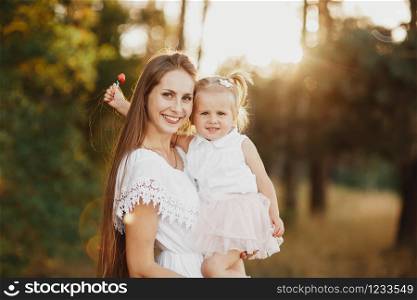 Lifestyle portrait mom and daughter in happines at the outside in the meadow. little girl with two tails.. Lifestyle portrait mom and daughter in happines at the outside in the meadow. little girl with two tails