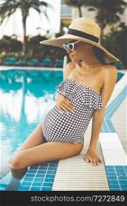 Lifestyle portrait of beautiful pregnant woman in straw hat in swimming pool. Beautiful pregnancy. Beauty and health