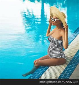 Lifestyle portrait of beautiful pregnant woman in straw hat in swimming pool. Beautiful pregnancy. Beauty and health