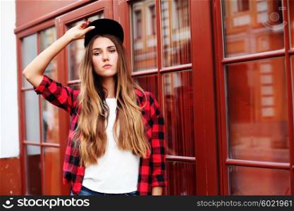 Lifestyle portrait of fashionable blonde girl with ombre hair wearing a rock red shirt, black cap, white t-shirt and denim shorts having fun outdoors in the city. Swag style.