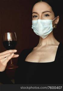 Lifestyle portrait of young beautiful lady in medical mask with glass of vine. Stay home. Coronavirus. Quarantine. Coronavirus pandemic in the world