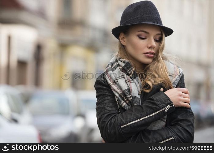 lifestyle shot of young pretty woman with scarf and hat , in urban situation , she has freckles on face . winter dress. she is looking down&#xA;