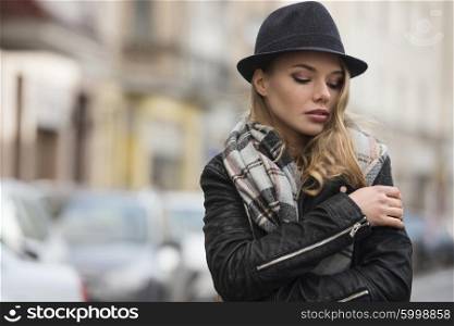 lifestyle shot of young pretty woman with scarf and hat , in urban situation , she has freckles on face . winter dress. she is looking down&#xA;