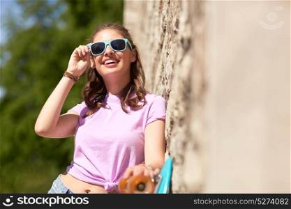 lifestyle, summer and people concept - smiling young woman or teenage girl in sunglasses with longboard over stone wall outdoors. happy teenage girl in shades with longboard
