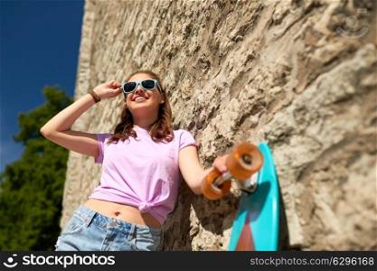 lifestyle, summer and people concept - smiling young woman or teenage girl in sunglasses with longboard over stone wall outdoors. happy teenage girl in shades with longboard