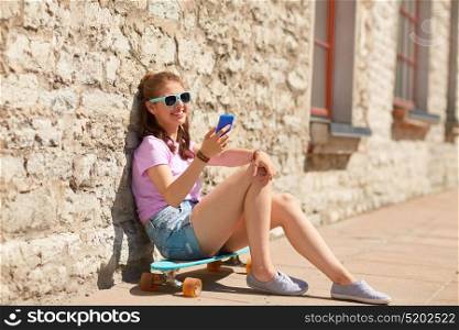 lifestyle, summer, technology and people concept - smiling young woman or teenage girl in sunglasses with longboard and smartphone over stone wall outdoors. happy teenage girl with longboard and smartphone