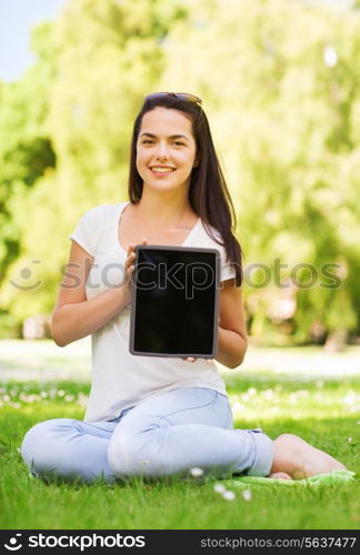 lifestyle, summer vacation, advertisement, technology and people concept - smiling young girl showing tablet pc screen and sitting in park