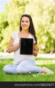 lifestyle, summer vacation, advertisement, technology and people concept - smiling young girl showing tablet pc screen and sitting in park
