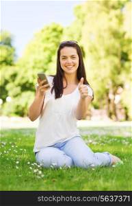 lifestyle, summer vacation, gesture, technology and people concept - smiling young girl with smartphone showing thumbs up in park