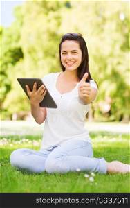 lifestyle, summer vacation, gesture, technology and people concept - smiling young girl with tablet pc showing thumbs up and sitting in park