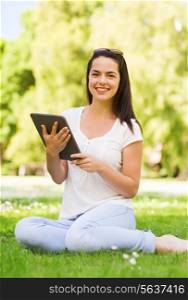 lifestyle, summer, vacation, technology and people concept - smiling young girl with tablet pc sitting on grass in park