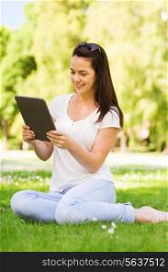 lifestyle, summer, vacation, technology and people concept - smiling young girl with tablet pc computer sitting on grass in park