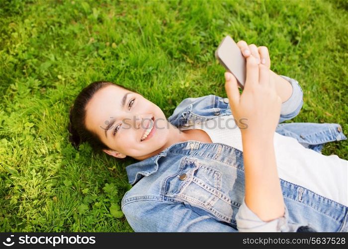 lifestyle, summer vacation, technology and people concept - smiling young girl with smartphone lying on grass in park