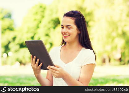 lifestyle, summer, vacation, technology and people concept - smiling young girl with tablet pc computer sitting on grass in park