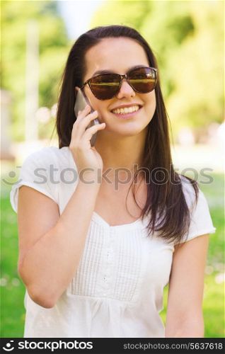 lifestyle, summer, vacation, technology and people concept - smiling young girl with smartphone calling in park
