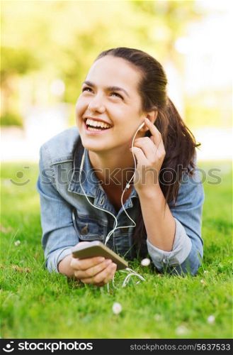 lifestyle, summer vacation, technology, leisure and people concept - laughingyoung girl with smartphone and earphones lying on grass