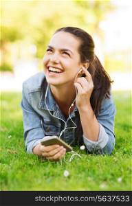 lifestyle, summer vacation, technology, leisure and people concept - laughingyoung girl with smartphone and earphones lying on grass