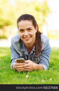 lifestyle, summer vacation, technology, leisure and people concept - smiling young girl with smartphone lying on grass in park