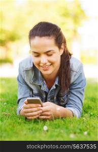 lifestyle, summer vacation, technology, leisure and people concept - smiling young girl with smartphone lying on grass in park