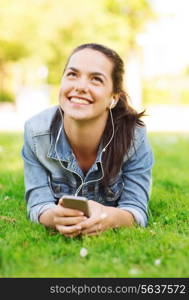 lifestyle, summer vacation, technology, leisure and people concept - smiling young girl with smartphone and earphones lying on grass