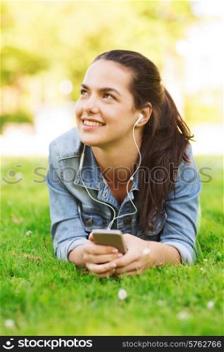 lifestyle, summer vacation, technology, leisure and people concept - smiling young girl with smartphone and earphones lying on grass