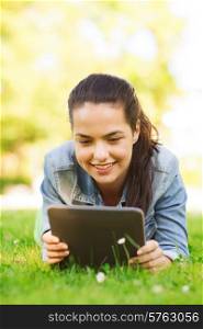 lifestyle, summer vacation, technology, leisure and people concept - smiling young girl with tablet pc computer lying on grass in park