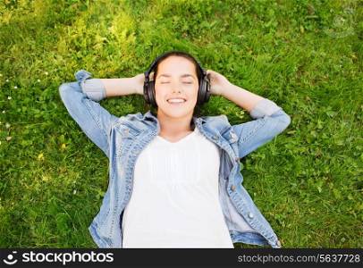 lifestyle, summer vacation, technology, music and people concept - smiling young girl in headphones lying with closed eyes on grass