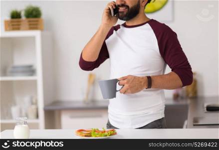 lifestyle, technology and people concept - man having sandwiches with coffee for breakfast and calling on smartphone at home kitchen. man calling on smartphone and eating at home