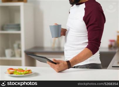 lifestyle, technology and people concept - man with tablet pc computer drinking coffee for breakfast at home kitchen. man with tablet pc eating at home kitchen