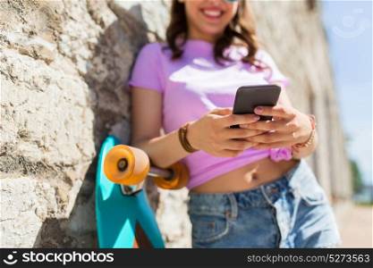 lifestyle, technology and people concept - smiling young woman or teenage girl in sunglasses with longboard and smartphone over stone wall outdoors. happy teenage girl with longboard and smartphone