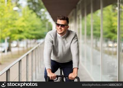 lifestyle, transport and people concept - happy smiling young man in sunglasses riding bicycle on city street